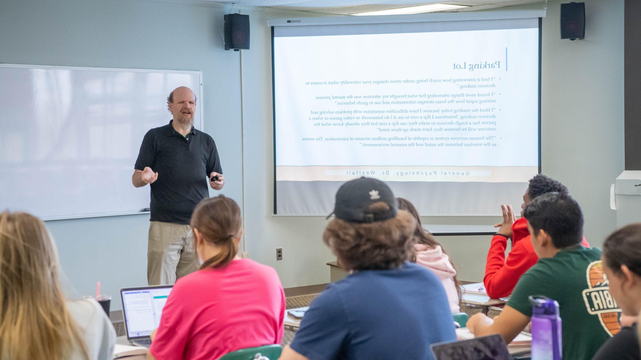 心理学教授站在课前，用投影仪屏幕上的PowerPoint演示文稿在学生面前讲课.