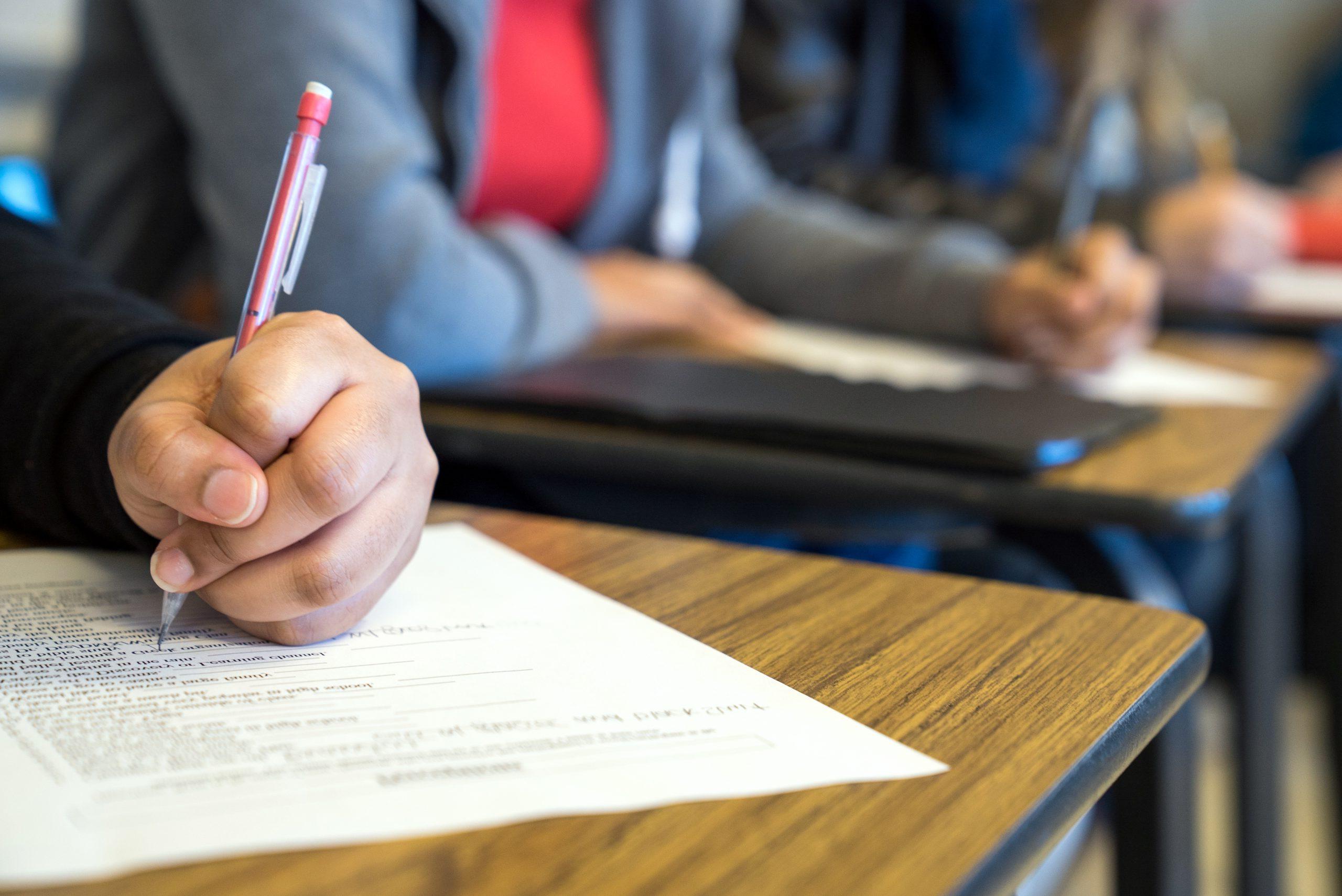 A students hand writing with a mechanical pencil on a handout given out during class.