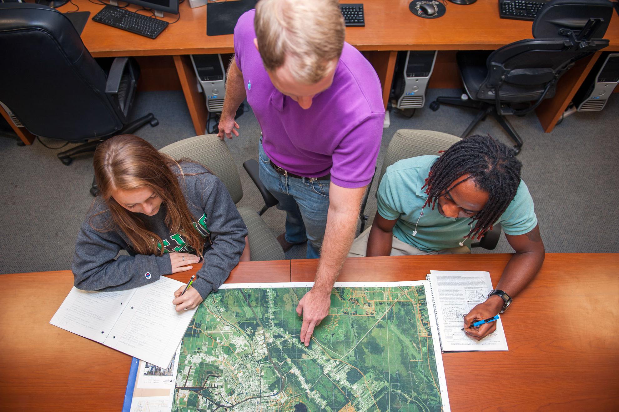 Instructor pointing at map on a table with two students on both sides of him.